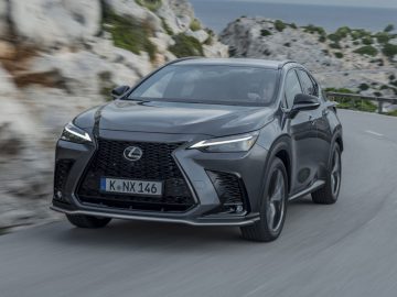 Een zilveren Lexus NX SUV, een betrouwbare auto, rijdt op een bochtige weg door een rotsachtig kustlandschap.