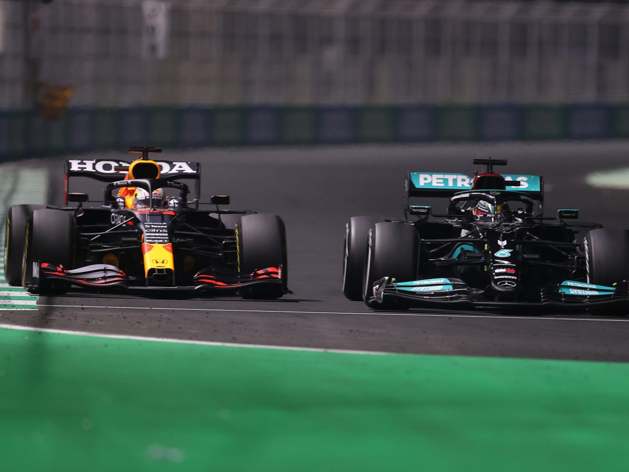 Twee Formule 1-auto's, die zich onderscheiden door hun levendige kleuren, racen zij aan zij op het circuit. De Honda-auto aan de linkerkant heeft een rode en gele kleurstelling, terwijl de zwarte Petronas-auto aan de rechterkant gelijke tred houdt. Het startnummer Formule 1 van elk voertuig draagt bij aan hun hevige concurrentie.