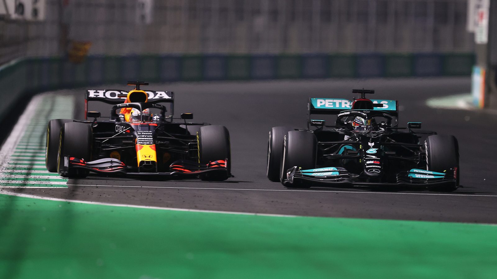 Twee Formule 1-auto's, die zich onderscheiden door hun levendige kleuren, racen zij aan zij op het circuit. De Honda-auto aan de linkerkant heeft een rode en gele kleurstelling, terwijl de zwarte Petronas-auto aan de rechterkant gelijke tred houdt. Het startnummer Formule 1 van elk voertuig draagt bij aan hun hevige concurrentie.