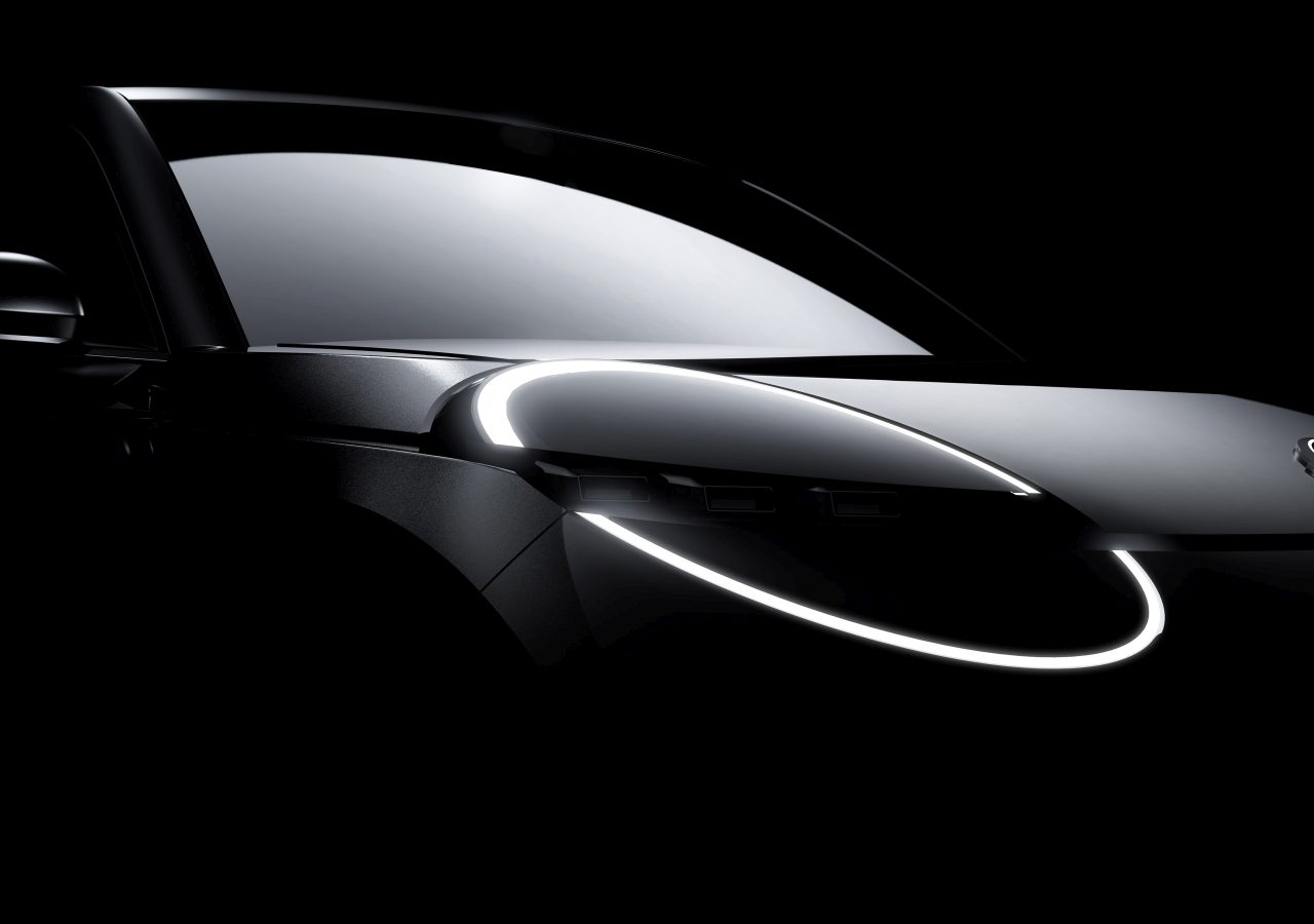 Een donker verlichte afbeelding van een moderne Nissan Micra met verlichte ringachtige LED-koplampen en een reflecterende voorruit. De auto is voorzien van strakke, afgeronde designelementen.