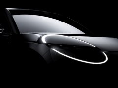 Een donker verlichte afbeelding van een moderne Nissan Micra met verlichte ringachtige LED-koplampen en een reflecterende voorruit. De auto is voorzien van strakke, afgeronde designelementen.