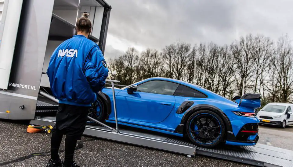 Een persoon in een NASA-jasje kijkt toe hoe een blauwe La Fuente-auto op een bewolkte dag op een transportwagen wordt geladen.