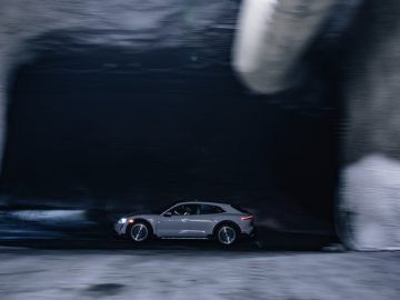 Een zilveren Porsche Taycan rijdt snel door een slecht verlichte tunnel, waardoor een gevoel van beweging ontstaat.