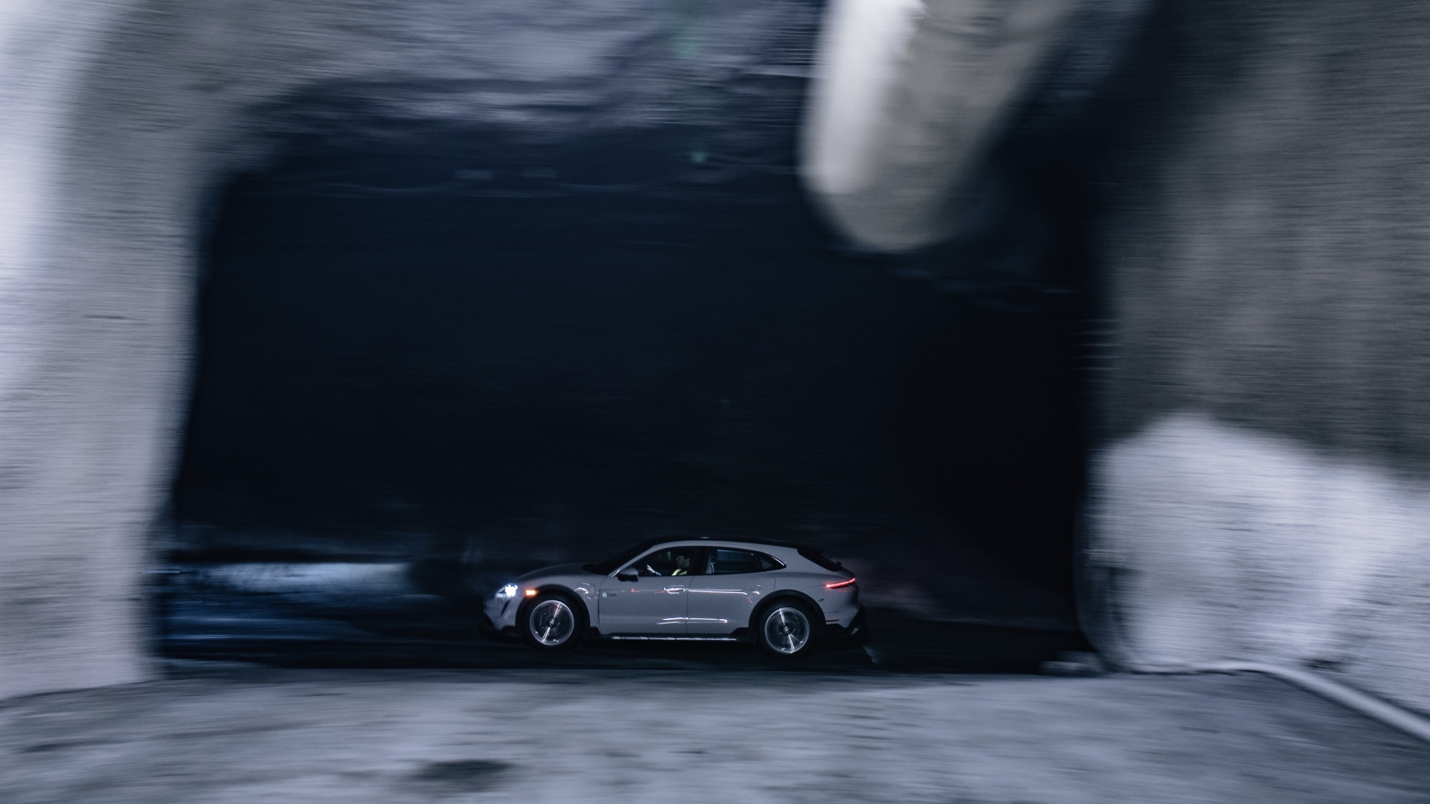 Een zilveren Porsche Taycan rijdt snel door een slecht verlichte tunnel, waardoor een gevoel van beweging ontstaat.