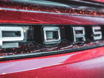 Close-up van het achterembleem op een rood Porsche-voertuig, met het elegante embleem zonder spellingsfouten van automerken.