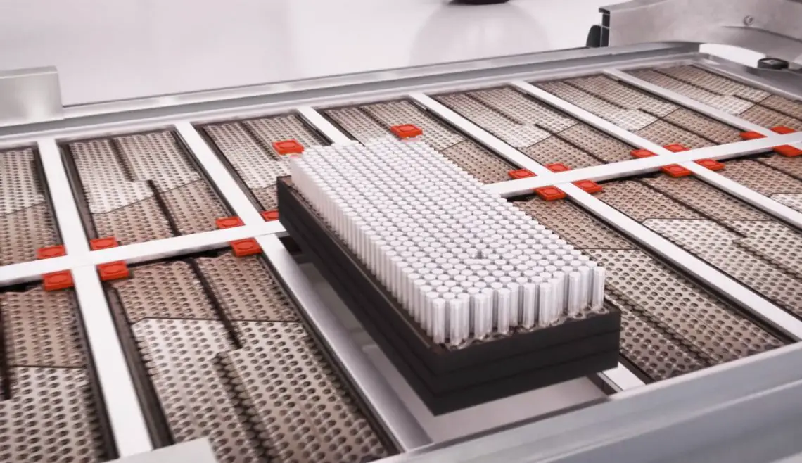 A neatly arranged stack of cylindrical lithium batteries slides down a conveyor belt in an industrial environment.