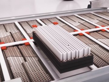 Een netjes gerangschikte stapel cilindervormige lithiumbatterijen glijdt over een lopende band in een industriële omgeving.