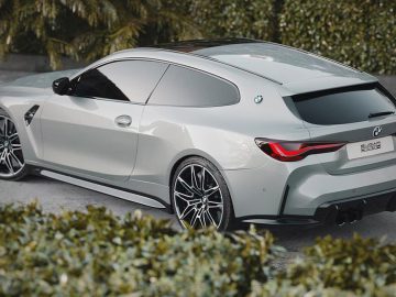 Op een verharde ondergrond, omgeven door groen, staat een strakke, zilveren BMW-sportwagen met getinte ramen geparkeerd. Het voertuig heeft een modern ontwerp met vloeiende rondingen en zwarte lichtmetalen velgen.