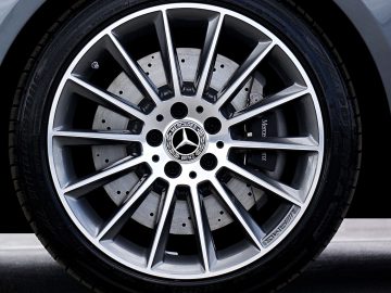 Close-up van een zilveren lichtmetalen velg met meerdere spaken, met het Mercedes-Benz-logo in het midden. De donkergrijze remschijf en het loopvlak van de band zijn zichtbaar op de achtergrond, wat de onberispelijke details laat zien na een grondige velgenreparatie.