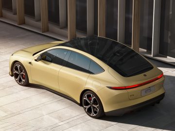 Een gouden auto met een strak ontwerp, getinte ramen en een panoramisch schuifdak staat geparkeerd op een verhard terrein nabij een modern gebouw. Op de achterkant van de NIO ET5 staat trots de modelnaam "et5".