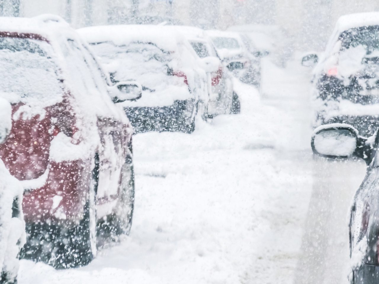 Met sneeuw bedekte elektrische auto geparkeerd langs een straat tijdens hevige sneeuwval.