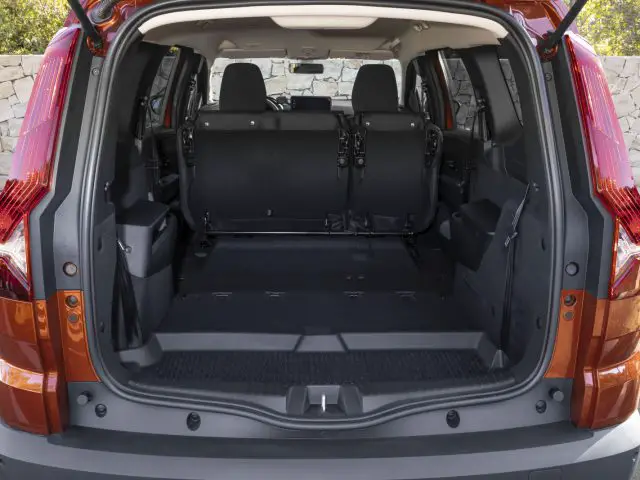 De afbeelding, wellicht afkomstig uit een Dacia Jogger-recensie, toont de open laadruimte van een oranje SUV met de achterbank neergeklapt, waardoor een ruim en leeg interieur zichtbaar wordt.