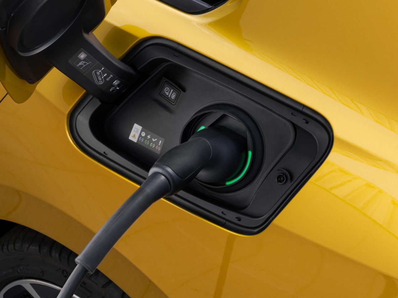 Close-up van de gele oplaadpoort voor elektrische auto's van een Opel Astra met een aangesloten oplaadkabel, aangegeven door een groen licht rond de connector.
