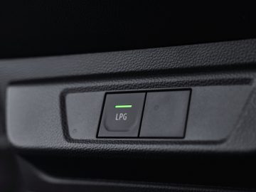 Close-up van de LPG-knop (vloeibaar petroleumgas) van een Dacia Jogger met een groen indicatielampje op een gestructureerd dashboard.