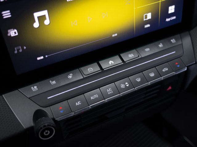 Close-up van een Opel Astra-dashboard met een touchscreen-display met muziekbediening en verschillende klimaatknoppen en pictogrammen.