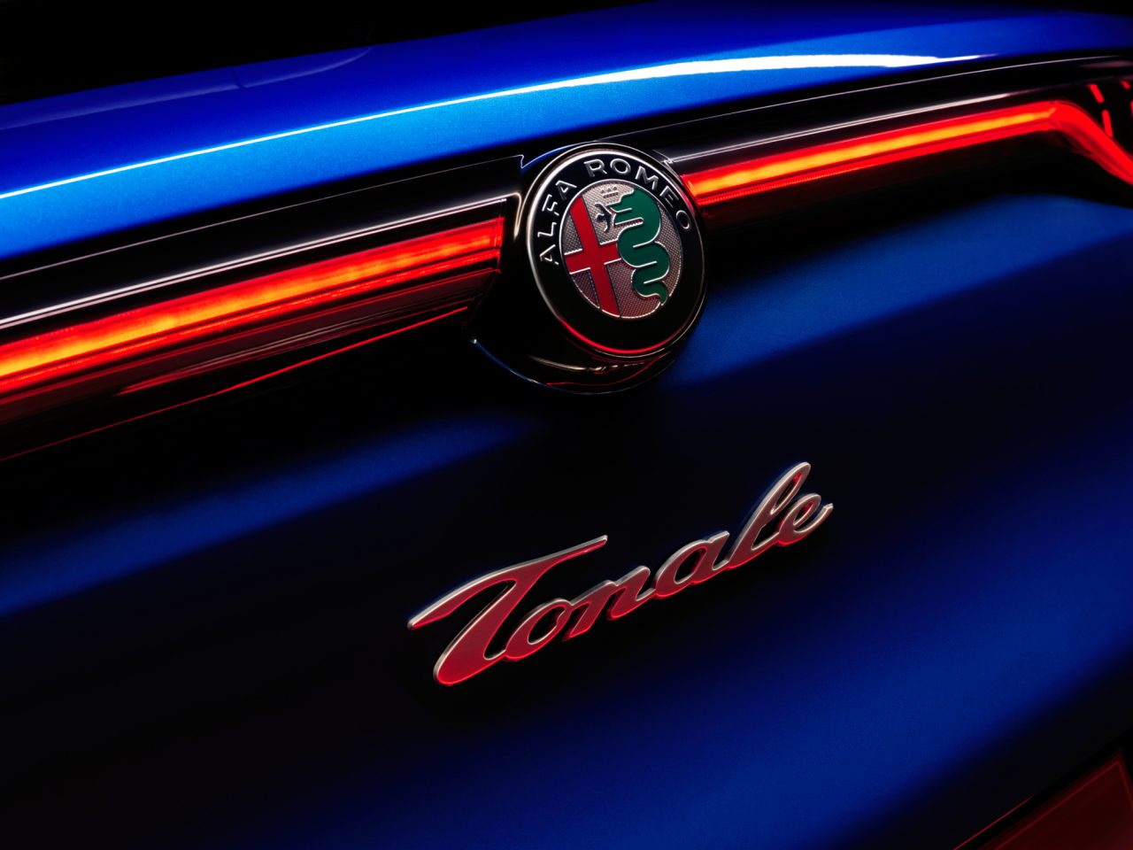 Close-up van het Alfa Romeo Tonale-embleem op de achterkant van een blauwe auto, verlicht door rode achterlichten.
