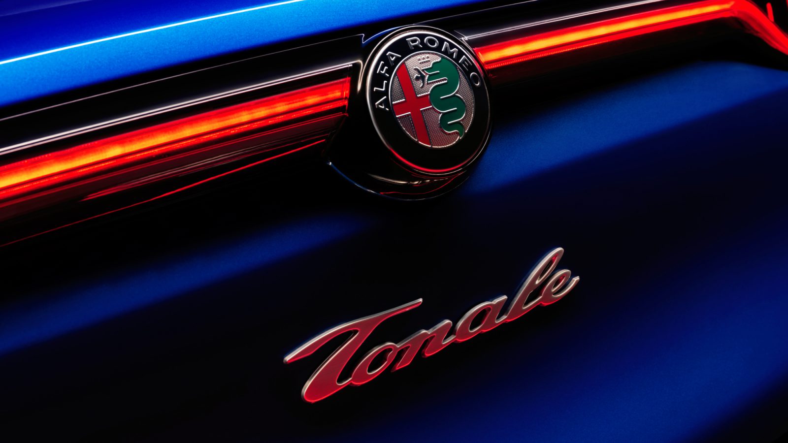 Close-up van het Alfa Romeo Tonale-embleem op de achterkant van een blauwe auto, verlicht door rode achterlichten.