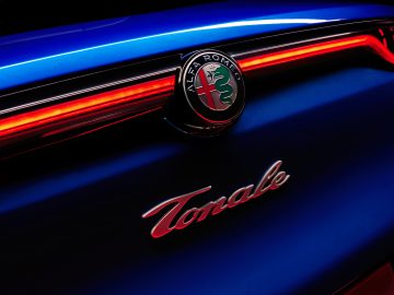 Close-up van het Alfa Romeo Tonale-embleem op de achterkant van een blauwe auto, verlicht door rode achterlichten.