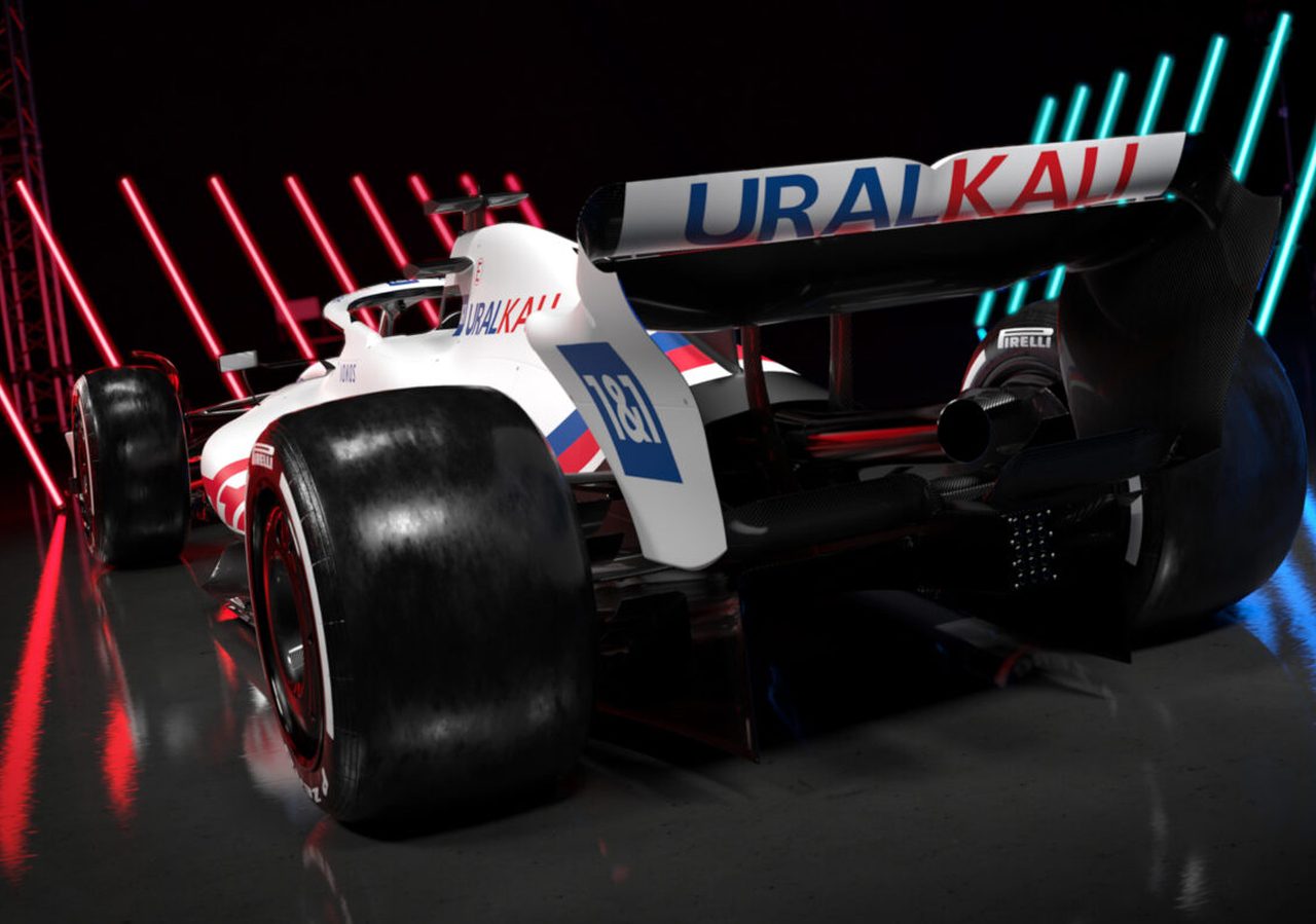 Een Formule 1-raceauto met het 'URALKALI'-logo op de achtervleugel wordt tentoongesteld in een slecht verlichte omgeving, verlicht door rode en blauwe neonlichten.