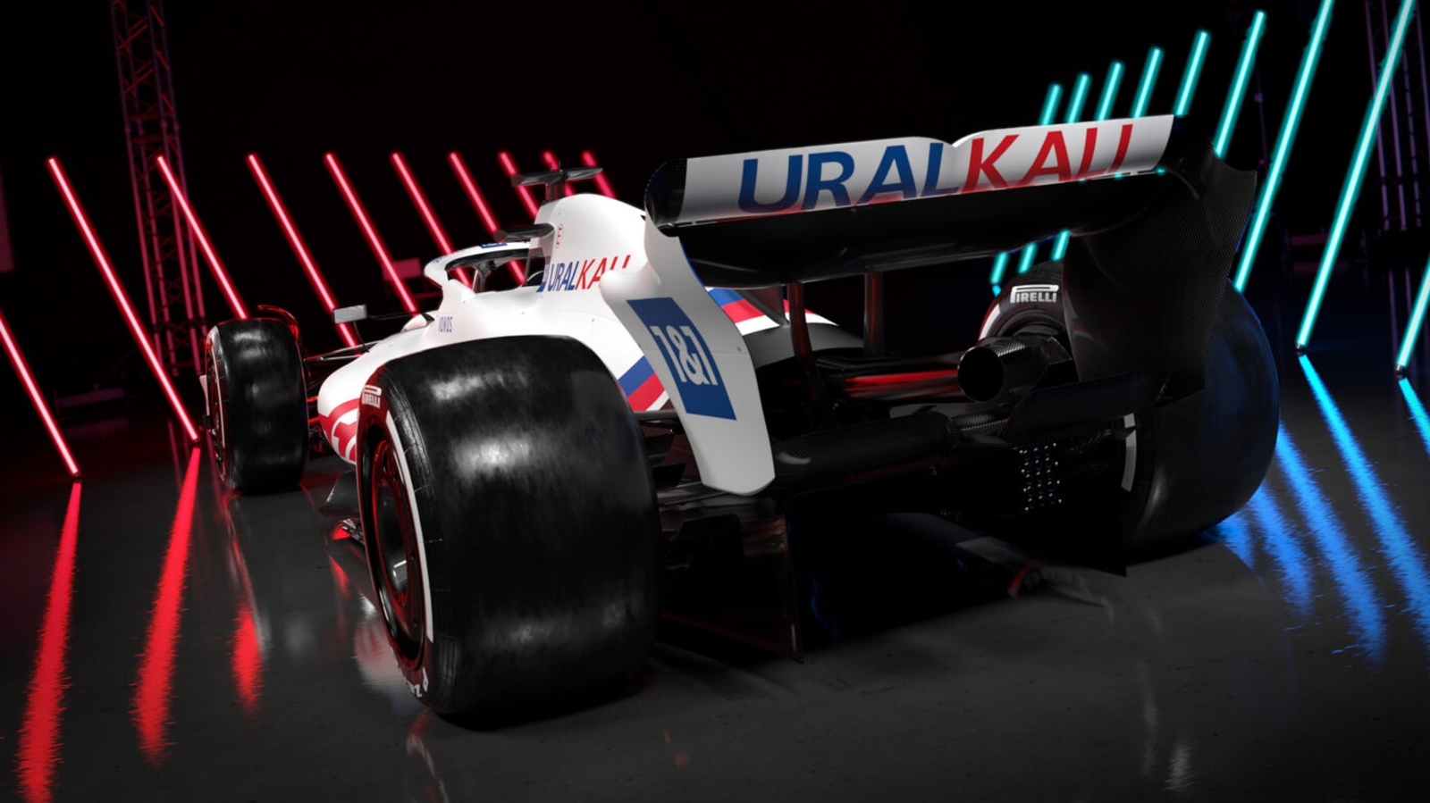 Een Formule 1-raceauto met het 'URALKALI'-logo op de achtervleugel wordt tentoongesteld in een slecht verlichte omgeving, verlicht door rode en blauwe neonlichten.