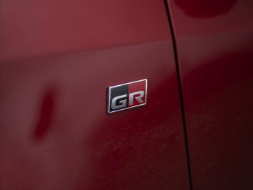 Close-up van de buitenkant van een rode Toyota GR Yaris met een badge met de letters "GR" in zwart en rood op de zijkant.