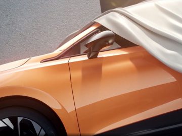 Een gedeeltelijk overdekte oranje elektrische auto met een wit laken over het dak en de zijspiegel gedrapeerd.