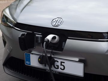 Er wordt een zilveren MG5 elektrisch voertuig getoond dat wordt opgeladen met een kabel die is aangesloten op de oplaadpoort aan de voorzijde.