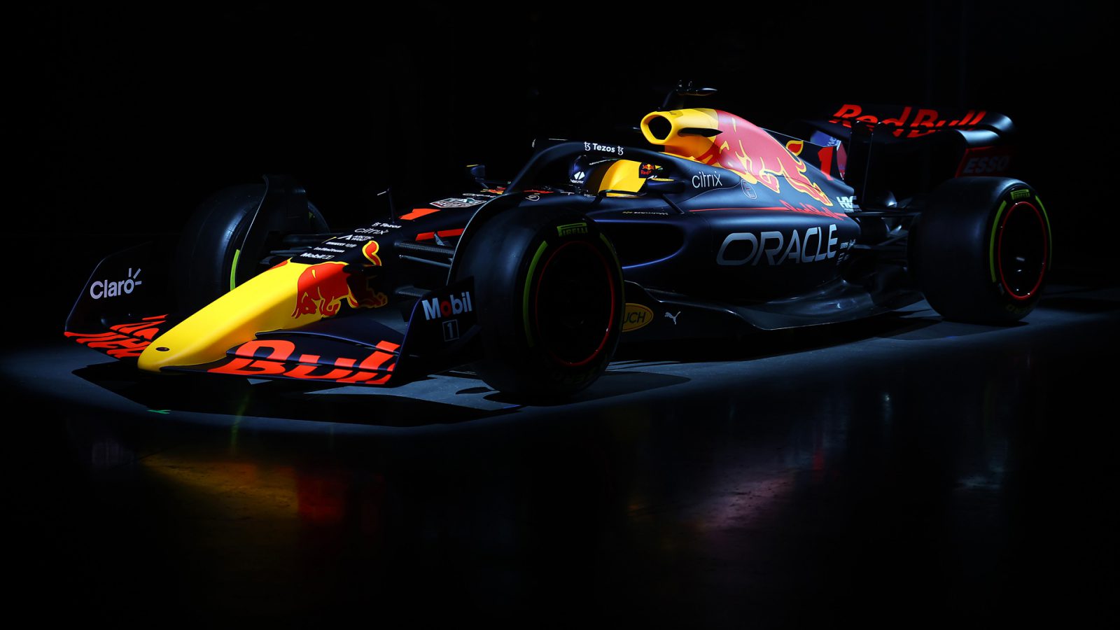 Een Formule 1-auto met een Red Bull Racing RB18-kleurstelling wordt in een donkere omgeving onder schijnwerpers getoond.