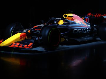 Een Formule 1-auto met een Red Bull Racing RB18-kleurstelling wordt in een donkere omgeving onder schijnwerpers getoond.