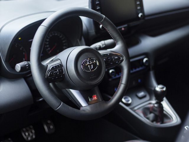 Binnenaanzicht van een Toyota GR Yaris met een zwart stuur met het Toyota-logo, een dashboard met een infotainmentscherm en een handmatige versnellingspook.