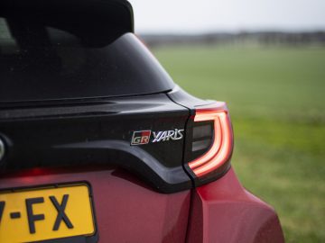 Close-up van een rode Toyota GR Yaris met het achterlicht, het GR Yaris-embleem en een deel van de kentekenplaat van het voertuig met de letters "7-FX" zichtbaar.