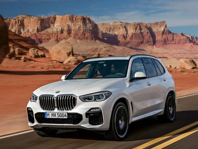 Een witte BMW waterstofauto SUV rijdt over een weg door een woestijn met grote rotsformaties op de achtergrond.