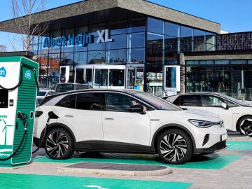Op een zonnige dag staan twee elektrische auto's geparkeerd bij snelladers buiten een Albert Heijn XL-supermarkt.