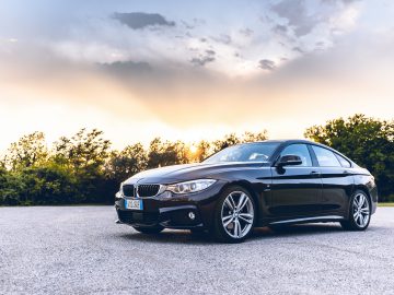 Op een verharde ondergrond staat een zwarte sedan, beschikbaar voor private lease, met een zonsondergang en bomen op de achtergrond.