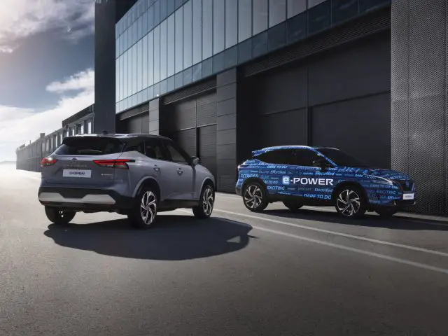Twee auto's geparkeerd voor een modern gebouw op een zonnige dag, met de auto aan de rechterkant trots gehuld in het Qashqai e-POWER-logo.
