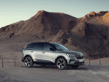 Een zilveren Renault Austral SUV staat overdag geparkeerd op een onverharde weg voor rotsachtige woestijnbergen.
