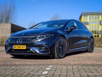 Een strakke zwarte Mercedes-Benz EQS sedan met kenteken N-788-HT staat op een heldere dag geparkeerd op een stenen stoep vlakbij een modern gebouw.