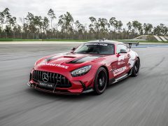 Een rode Mercedes-AMG safety car, versierd met 'Crowdstrike', rijdt op een racecircuit omgeven door bomen. Het gestroomlijnde voertuig is een vaste waarde tijdens Formule 1-evenementen en zorgt voor soepele en veilige raceomstandigheden.