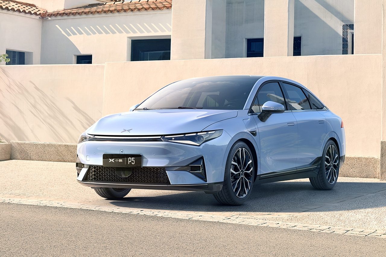 Een lichtblauwe Xpeng-sedan staat op een zonnige dag geparkeerd voor een modern wit gebouw. Op het kenteken van de auto staat "P5".