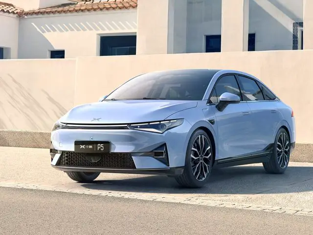 Een lichtblauwe Xpeng-sedan staat op een zonnige dag geparkeerd voor een modern wit gebouw. Op het kenteken van de auto staat