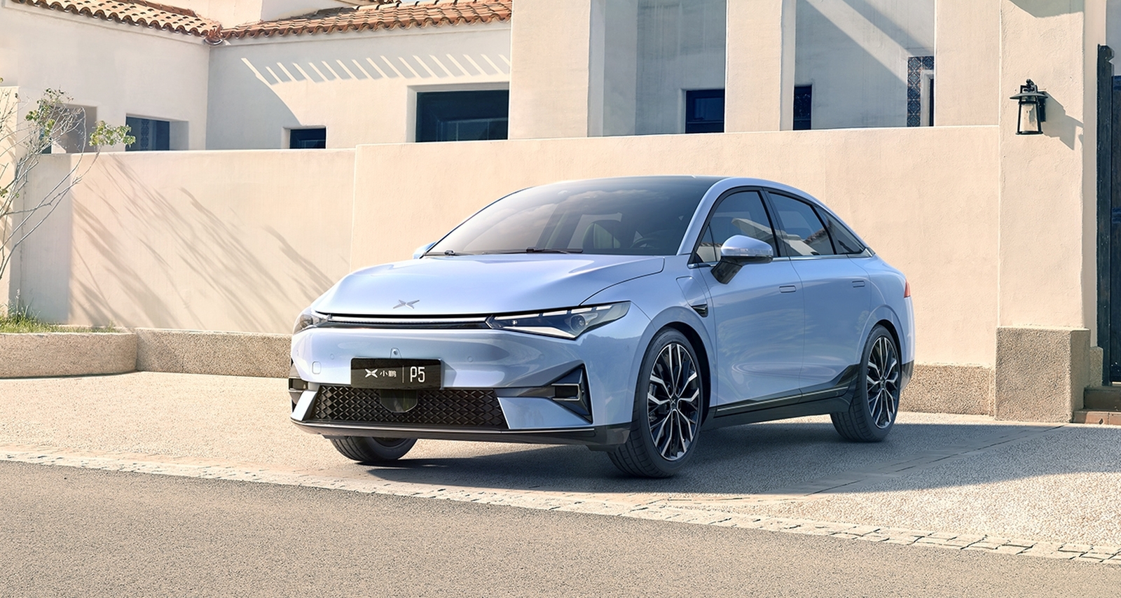 Een lichtblauwe Xpeng-sedan staat op een zonnige dag geparkeerd voor een modern wit gebouw. Op het kenteken van de auto staat "P5".
