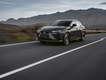 Een zwarte Lexus RZ 450e SUV rijdt op een snelweg met bergen op de achtergrond onder een gedeeltelijk bewolkte hemel.
