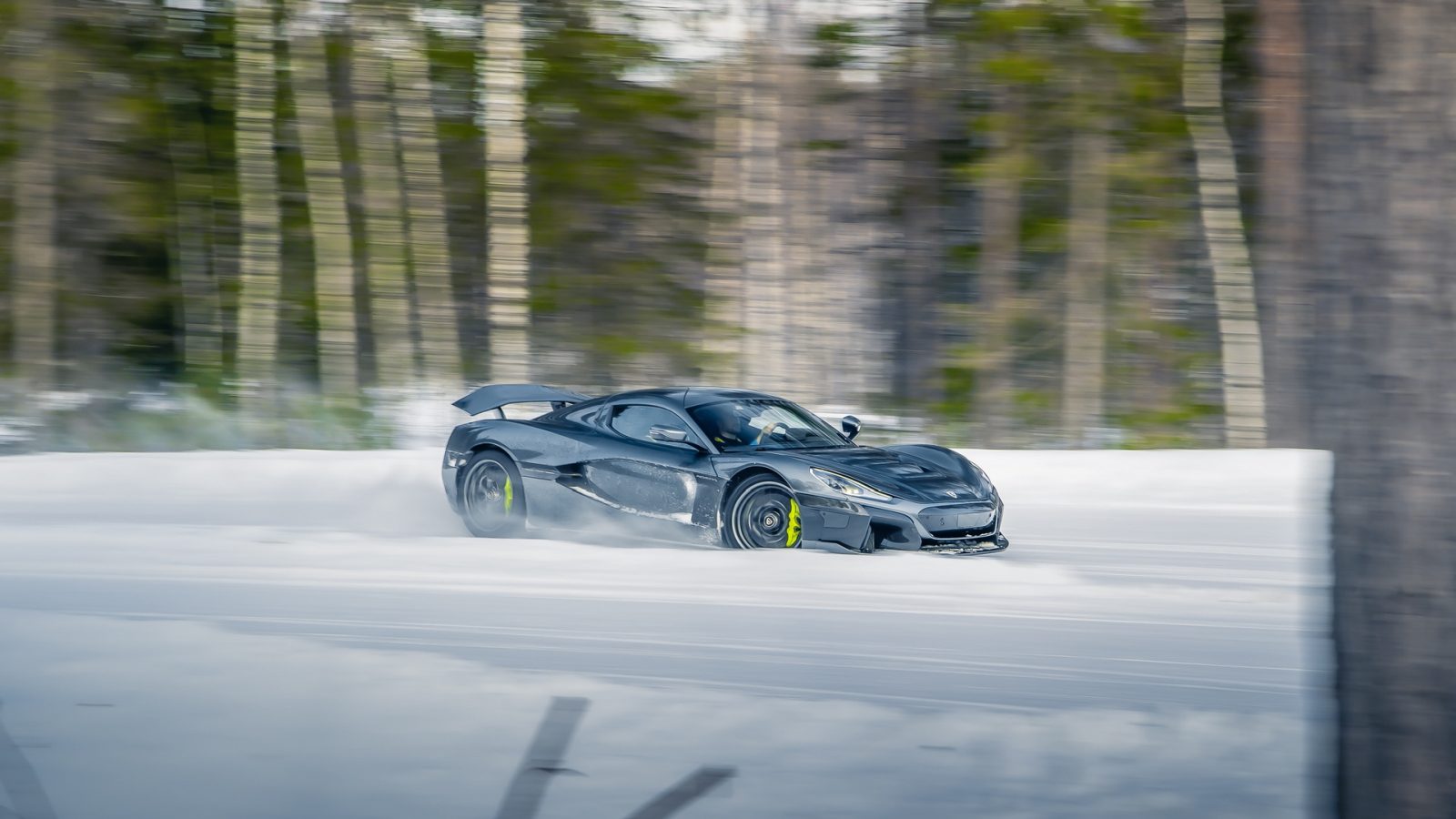 Een slanke zwarte Rimac Nevera drijft moeiteloos over een besneeuwde bosweg, met een ongeëvenaarde precisie. Bomen op de achtergrond zijn enigszins wazig, wat beweging aangeeft.