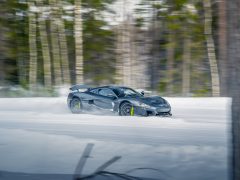 Een slanke zwarte Rimac Nevera drijft moeiteloos over een besneeuwde bosweg, met een ongeëvenaarde precisie. Bomen op de achtergrond zijn enigszins wazig, wat beweging aangeeft.