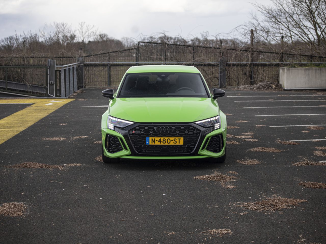 Een felgroene Audi RS 3 met kenteken "N-480-ST" staat geparkeerd op een lege parkeerplaats buiten.