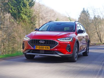 Een rode Ford Focus met een P-588-HN-kentekenplaat rijdt op een weg omgeven door bomen.