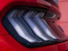 Close-up van het achterlicht van een moderne Ford Mustang met een hoekig, strak ontwerp. De auto is rood gespoten.