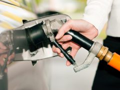 De hand van een persoon houdt een brandstofmondstuk vast en steekt deze in de brandstoftank van een auto om benzine te tanken.