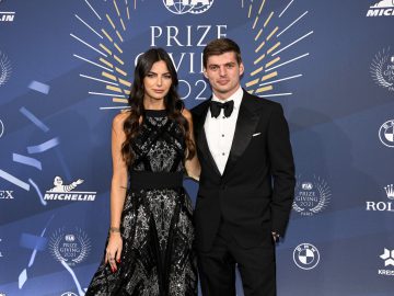 Twee personen gekleed in formele kledij, waaronder Kelly Piquet, staan samen op een blauwe loper tijdens een FIA-prijsuitreiking. Op de achtergrond staan logo's van verschillende sponsors en de titel van het evenement "PRIZE GIVING 2021.