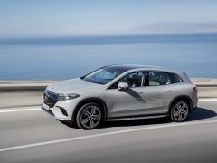 Een zilveren Mercedes EQS SUV rijdt op een heldere dag over een kustweg met de oceaan op de achtergrond.